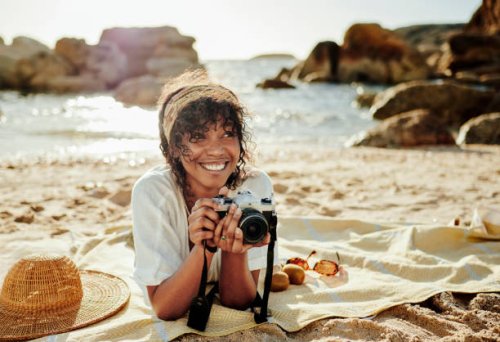 smiling young woman taking photos while relaxing on a sandy beach - travel stock pictures, royalty-free photos & images