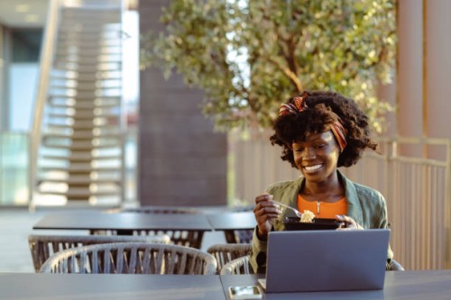smiling young woman using laptop during the lunch break - junk food stock pictures, royalty-free photos & images