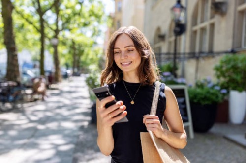 smiling young woman with smartphone walking on the street - fashion stock pictures, royalty-free photos & images