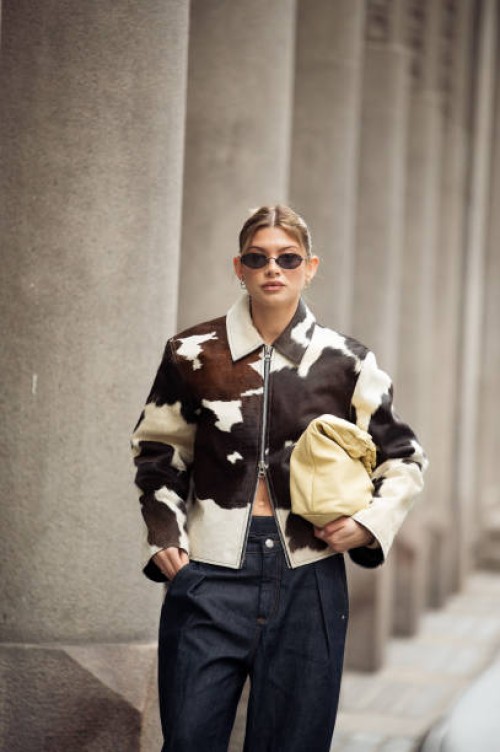 Sophia Geiss wears cow print cropped jacket with a zipper, pale yellow bag, blue wide jeans during the Copenhagen Fashion Week Autumn/Winter 2025 on...