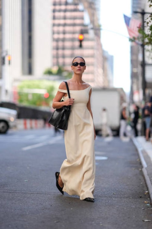 Sophia Roe wears black sunglasses, white off the shoulder maxi dress, shiny black leather bag, outside Toteme, during the New York Fashion week...