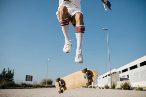 sportive man jumping above ground with skateboard performing trick - fashion stock-fotos und bilder