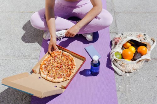 sportswoman having pizza while sitting cross-legged on exercise mat - junk food stock pictures, royalty-free photos & images