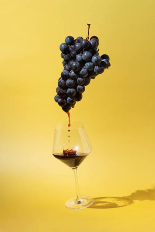 still life with black grapes and flowing red wine into a glass on yellow background - food stock pictures, royalty-free photos & images