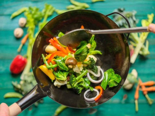 stir frying and sauteing a variety of fresh colorful market vegetables in a hot steaming wok with vegetables on on a turquoise colored wood table background below the wok. - food stock pictures, royalty-free photos & images