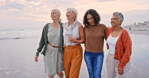 strand, freunde und urlaub mit einer älteren frauengruppe, die auf dem sand am meer oder ozean spazieren geht. natur, wasser und freundschaft mit vielfalt und reifen weibchen, die bei sonnenuntergang in ihrem ruhestand lachen