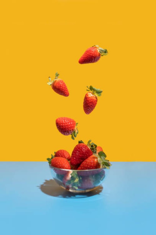 strawberries flying in the bowl on the blue-yellow background - food stock pictures, royalty-free photos & images