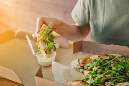 stylish girl adds sauce to a slice of vegetarian pizza. italian cuisine. sliced pizza in paper packaging on a wooden table. delicious lunch, snack, fast food. - junk food stock pictures, royalty-free photos & images