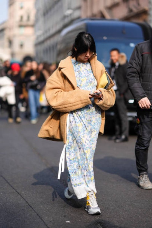 Susie Lau wears a beige wool jacket, a white and blue floral prints dress, a yellow leather bag, outside Onitsuka Tiger , during the Milan Fashion...