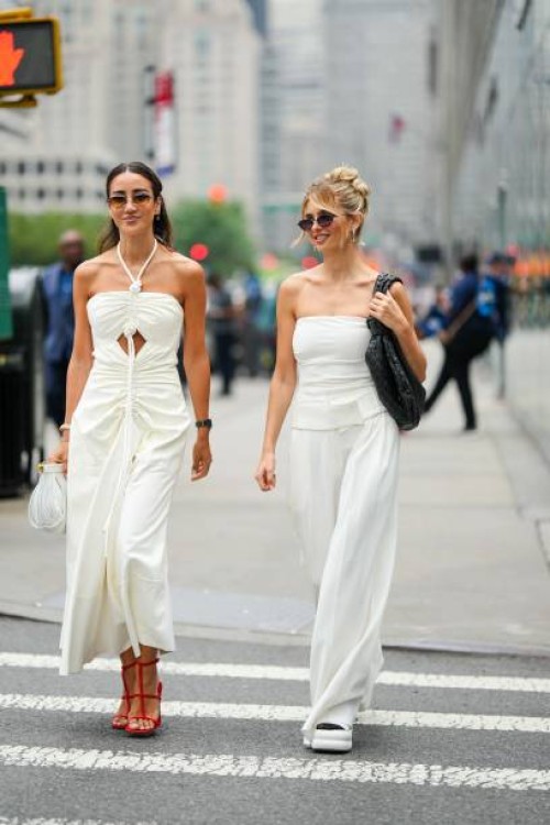 Tamara Kalinic wears a white gathered dress ; Xenia Adonts wears a white off-shoulder top, white palazzo flared pants, outside Proenza Schouler,...