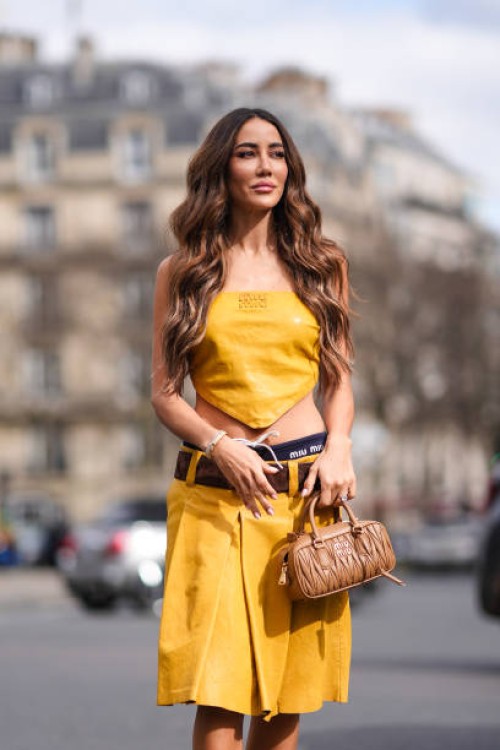 Tamara Kalinic wears a yellow off-shoulder cropped top, a brown leather belt, a leather knee-length skirt , a brown leather bag, outside Miu Miu ,...
