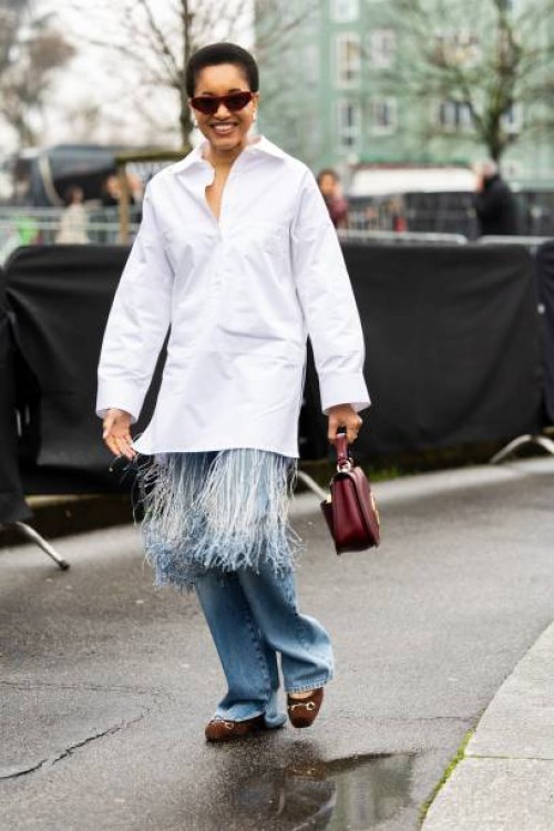 Tamu McPherson wears bordeaux sunglasses, silver hoop earrings, a white oversized shirt with fringes, a bordeaux Gucci leather bag, blue jeans and...
