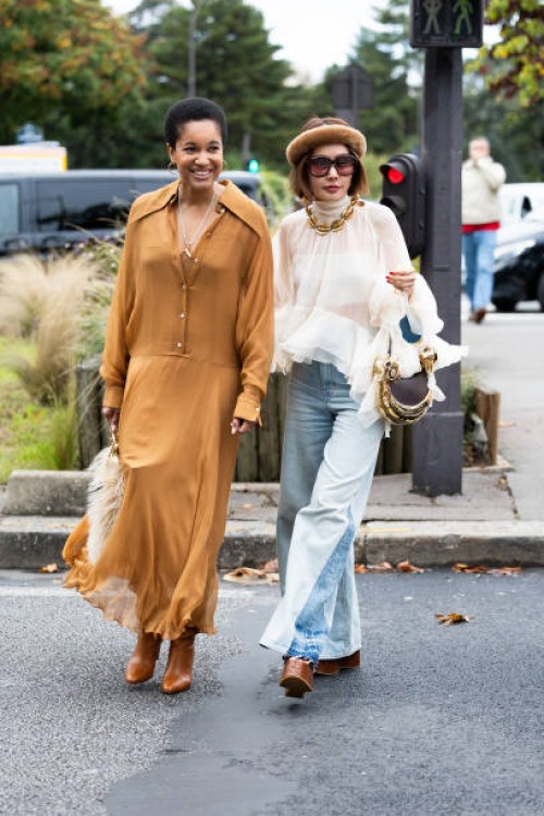Tamu McPherson wears gold hoop earrings, a brown and beige fur bag, a beige long sleeved long shirt dress and brown leather heeled boots and on the...