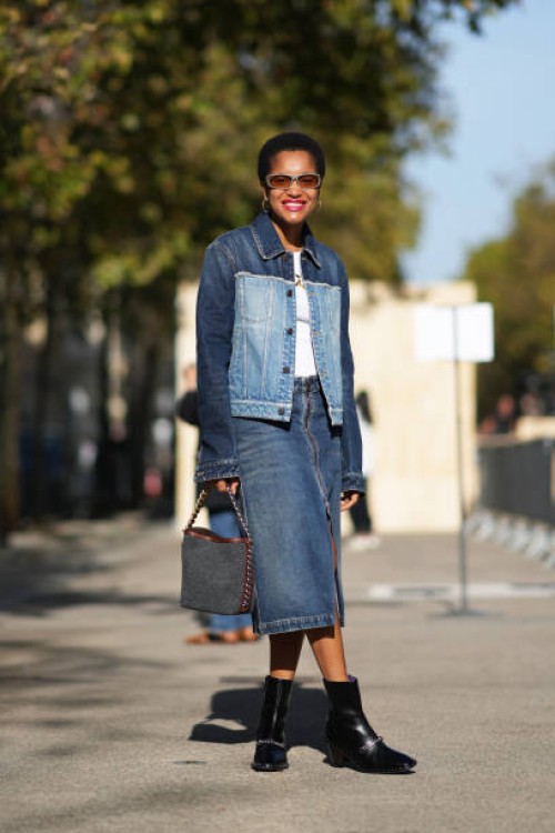 Tamu McPherson wears sunglasses, a bi-color dark blue and pale blue denim jacket, a white t-shirt, a blue slit denim skirt, a bag, black leather...