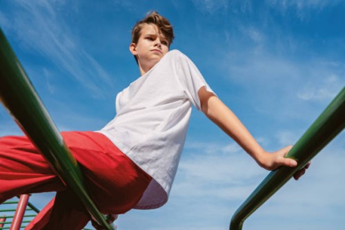 teen boy in sports wear outdoors sits on bars against blue sky - fashion stock pictures, royalty-free photos & images