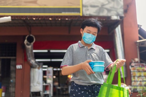 teenage boy buying takeout food from a restaurant using reusable food container - junk food stock pictures, royalty-free photos & images