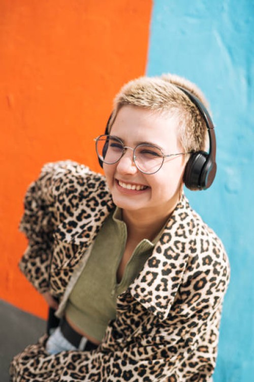 teenage girl with short hair in leopard jacket with headphones listens to music against bright wall - fashion stock pictures, royalty-free photos & images