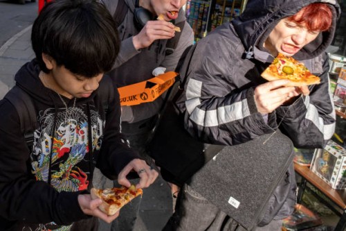 Teenagers eating pizza on the street on 15th November 2024 in Shrewsbury, United Kingdom. Shrewsbury is a market town, civil parish and the county...