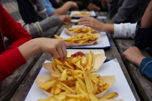 teenagers sitting at a picnic table eating takeaway fast food chips in paper trays - junk food stock pictures, royalty-free photos & images