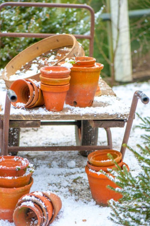 terracotta orange garden flower pots/containers and a garden sieve on a trolley in the winter snow - garden decoration stockfoto's en -beelden