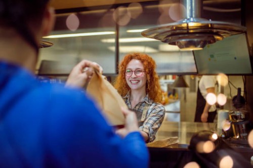 the cheerful waitress has prepared the delivery orders and gives them to the delivery man. - junk food stock pictures, royalty-free photos & images