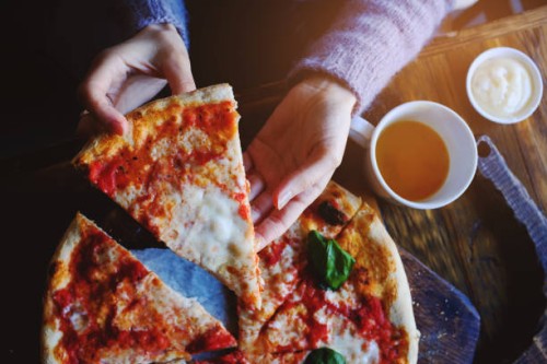 the girl takes a piece of vegetarian pizza with mozzarella cheese, tomatoes, spices and fresh basil. delicious italian food. sliced pizza margarita on a wooden board. close up. delicious lunch, snack - junk food stock picture