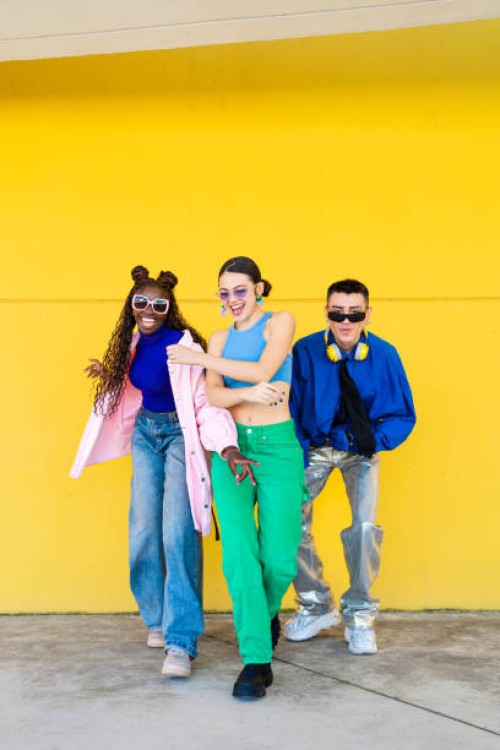 three fashionable young adults are posing and smiling against a vibrant yellow wall, showcasing their unique style - fashion stock pictures, royalty-free photos & images