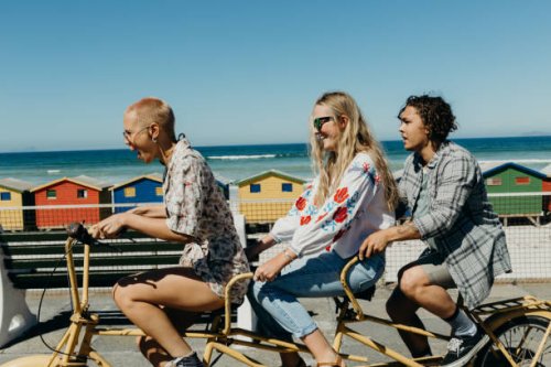 three friends laughing on a tandem bicycle on a boardwalk - travel stockfoto's en -beelden