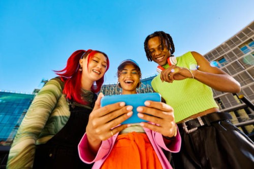three gen z friends using a smartphone together. low angle shot with modern buildings in the background. social media and friendship concept. - fashion stock pictures, royalty-free photos & images