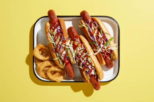 three hotdogs on tray with onion rings, overhead view on yellow background - junk food stock pictures, royalty-free photos & images