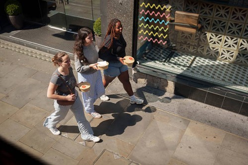 Three work colleagues bring identical takeaway lunches along the street, on 29th April 2025, in London, England.