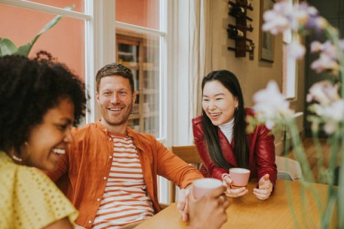 three young people sit around a table and giggle as they have a lighthearted discussion and drink coffee / tea - coffee stock pictures, royalty-free photos & images