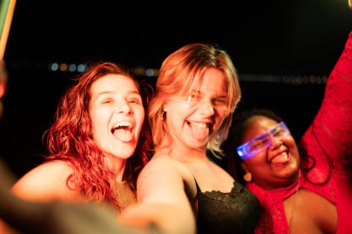 three young women taking selfie sticking out tongues at night - concert stock pictures, royalty-free photos & images