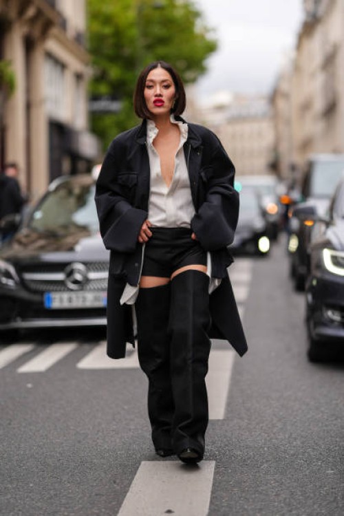 Tiffany Hsu wears white half unbuttoned shirt, black mini shorts, black oversized jacket, black thigh high heeled leather boots, outside Sacai,...