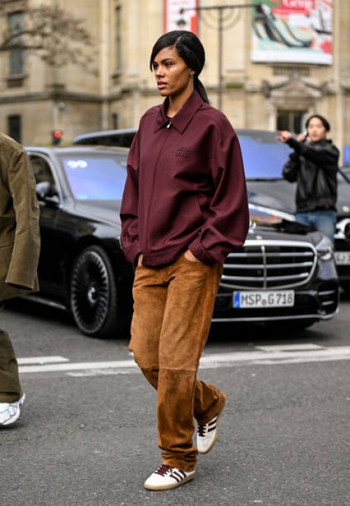Tina Kunakey is seen wearing a maroon Miu Miu jacket, brown pants and white and black stripe sneakers outside the Miu Miu show during the Womenswear...