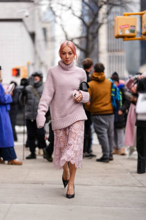 Tina Leung wears gold earrings, light pink turtleneck knit Michael Kors sweater, silver rings, light pink sheer mesh floral Michael Kors midi skirt,...