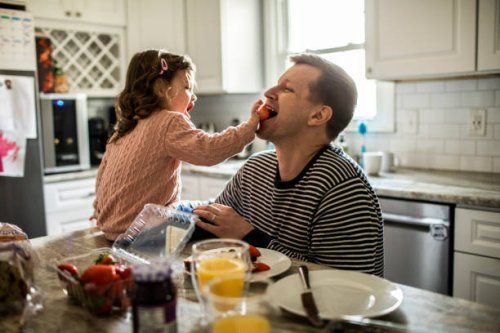 toddler girl feeding her father a strawberry in kitchen - food stock pictures, royalty-free photos & images