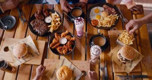 top view, hands and fast food on table at restaurant for dinner or lunch, people with cuisine and catering. burger, fries and milkshake drinks with wings for nutrition and eating meal for supper - food stock pictures, royalty