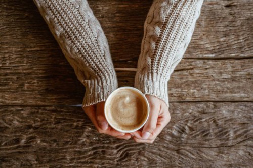 top view of woman hands holding a cup of hot milk coffee before drinking on wooden table. - coffee stock pictures, royalty-free photos & images