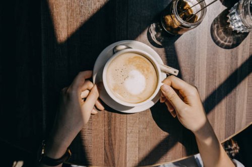 top view of woman sitting by the window in coffee shop enjoying the warmth of sunlight and drinking coffee - coffee stockfoto's en -beelden