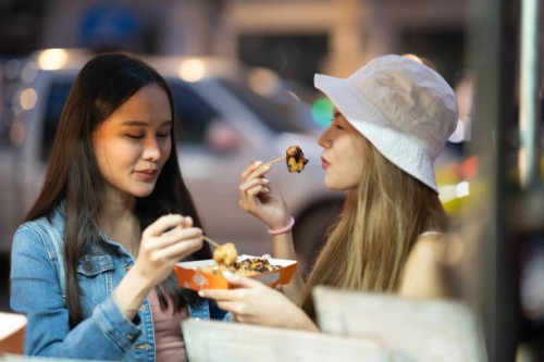 tourist women enjoyment eating snack street food in famous street night marke - junk food stock pictures, royalty-free photos & images