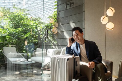 travelling asian businessman smiles at an airport lounge after receiving great news over the phone - travel stock pictures, royalty-free photos & images