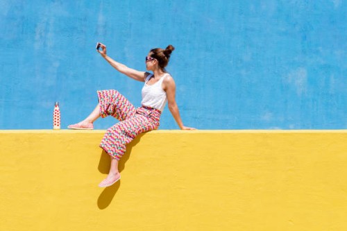trendy woman sitting on yellow wall while taking a selfie - fashion stock pictures, royalty-free photos & images