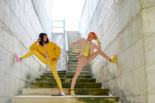 two alternative friends posing on steps, wearing yellow and pink jeans clothes - fashion stock pictures, royalty-free photos & images
