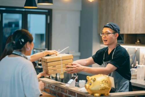 two asian customers come to pick up their take-out pizzas, and the pizza shop owner personally hands over the ordered meals to them. - junk food stock pictures, royalty-free photos & images