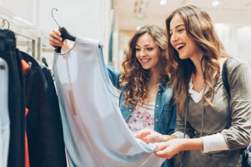 two cheerful girls shopping for clothes - fashion stock pictures, royalty-free photos & images