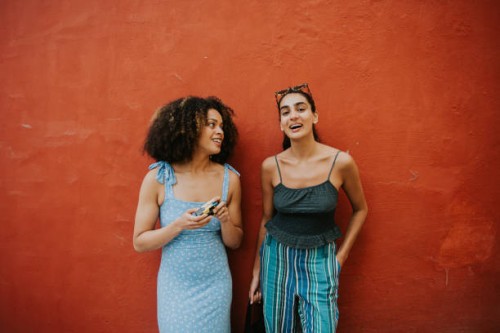 two fashionable young woman stand against a bright red wall - fashion fotografías e imágenes de stock