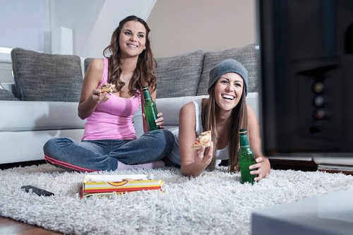 two female friends side by side on carpet at home watching television - junk food stock pictures, royalty-free photos & images