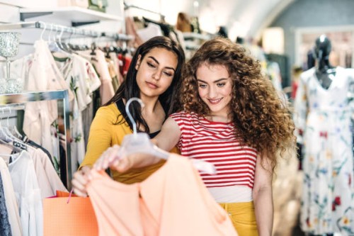 two female teenager friends standing inside in the shop, holding and looking at dress. - fashion stock pictures, royalty-free photos & images