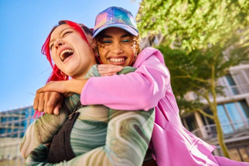 two gen z adults hugging and smiling outdoors in an urban environment. close-up shot. - fashion stock pictures, royalty-free photos & images